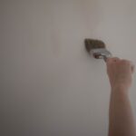 Jak odświeżyć stary korytarz niskim kosztem: malowanie, wymiana uchwytów i szybkie metamorfozy Ręka malująca ścianę pędzlem podczas odświeżania korytarza